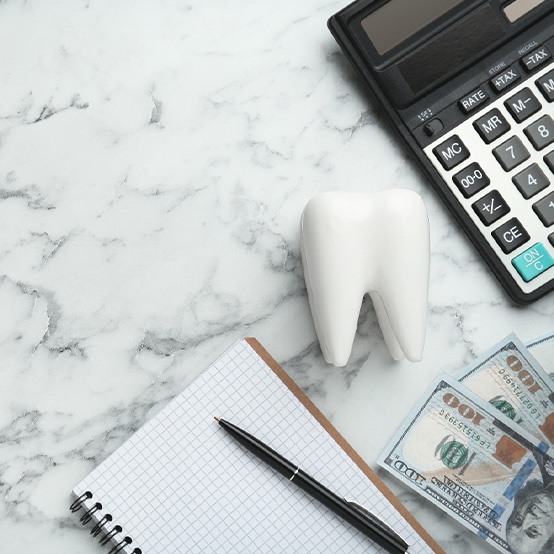 Model tooth, notebook, pen, $100 bills, and calculator on marbled surface
