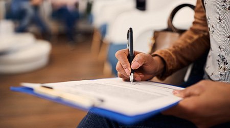 Someone in waiting room filling out forms on clipboard