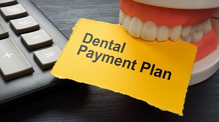 Artificial teeth biting yellow paper that says “Dental Payment Plan”