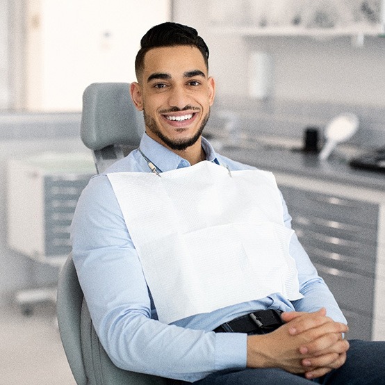 Bearded male patient sitting in dental chair smiling with hands folded