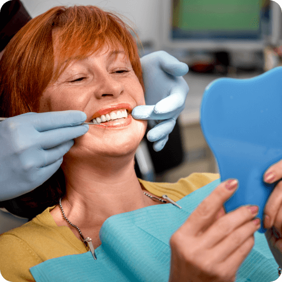 Woman looking at smile in mirror after getting dental implants in Eugene