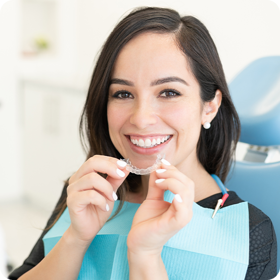 Smiling woman holding Reveal clear aligner for orthodontics in Eugene