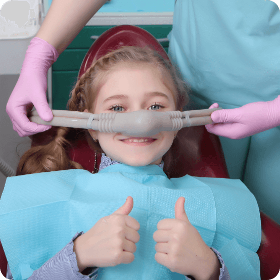 Child giving thumbs up as dentist places a nitrous oxide dental sedation mask